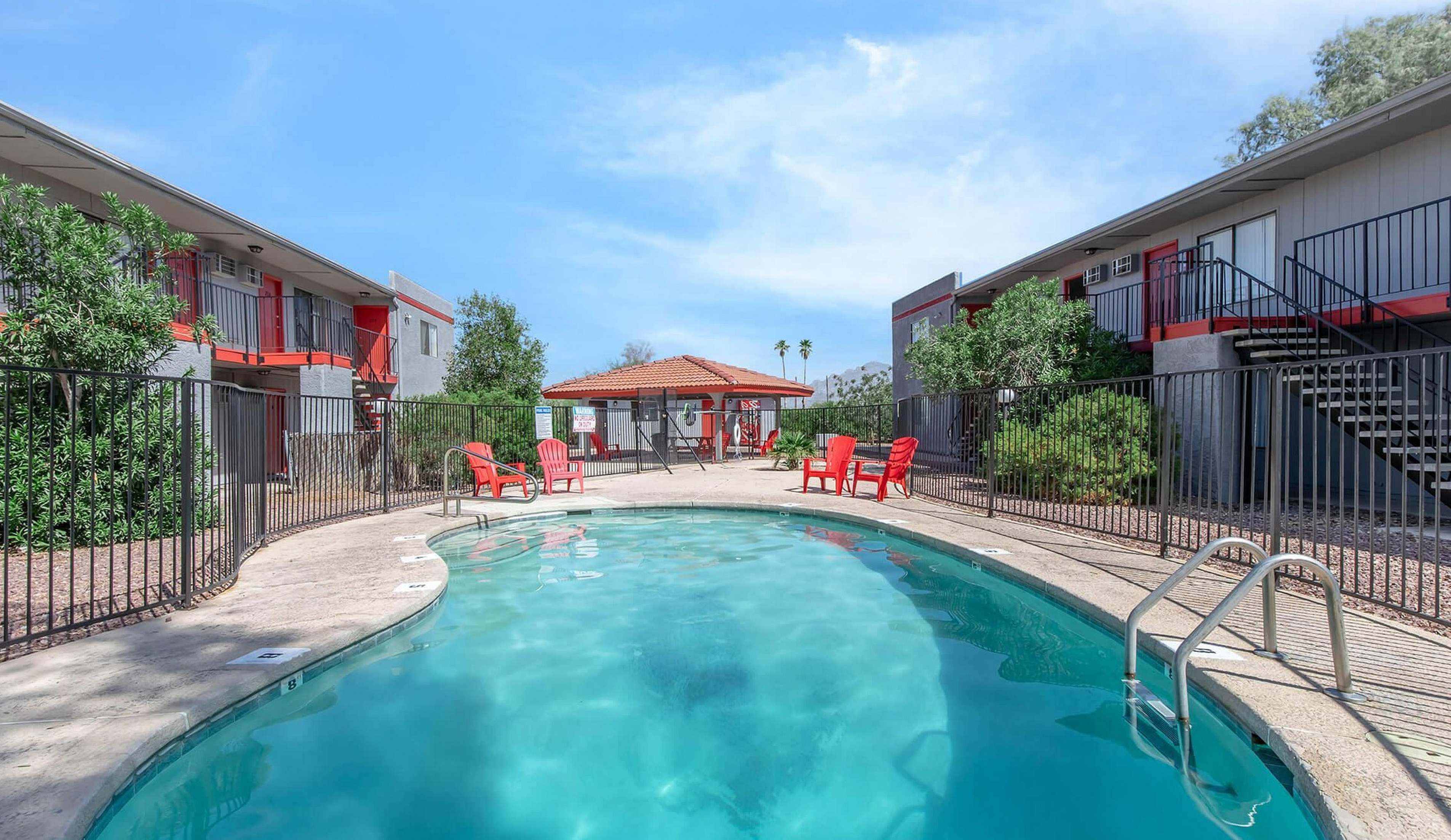 Inviting apartment courtyard with a sparkling pool surrounded by vibrant red chairs, lush greenery, and charming architecture.