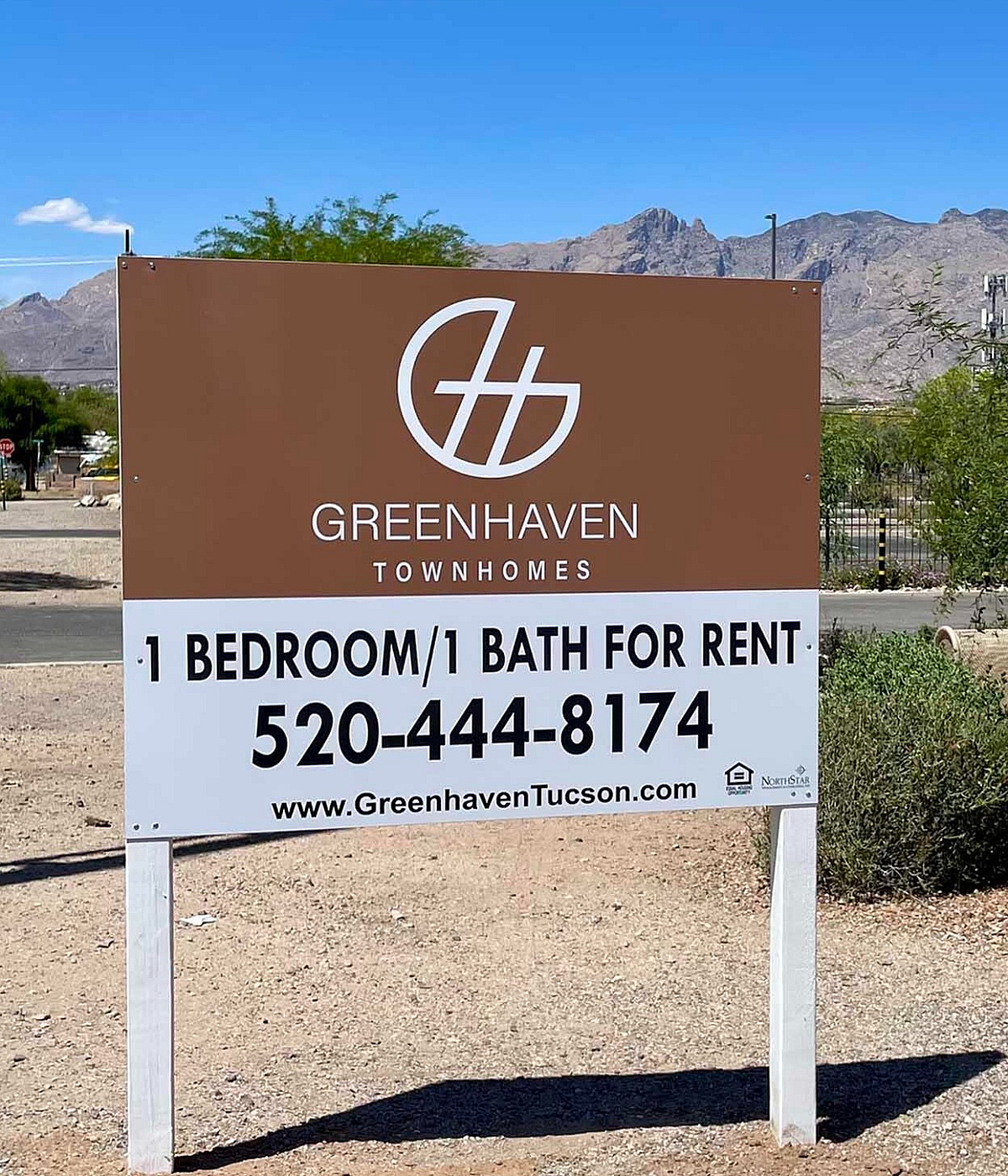 Greenhaven Townhomes sign offering 1 bedroom, 1 bath rentals, set against a backdrop of scenic mountains and clear skies.