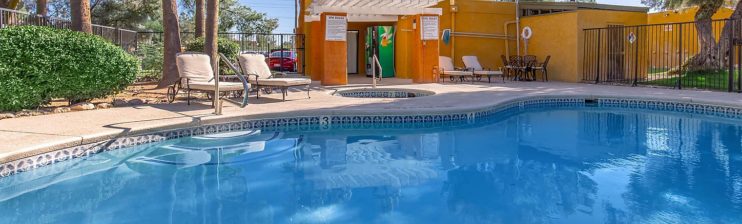 Inviting outdoor pool surrounded by lush greenery and palm trees, featuring sun loungers and a vibrant clubhouse in a serene setting.