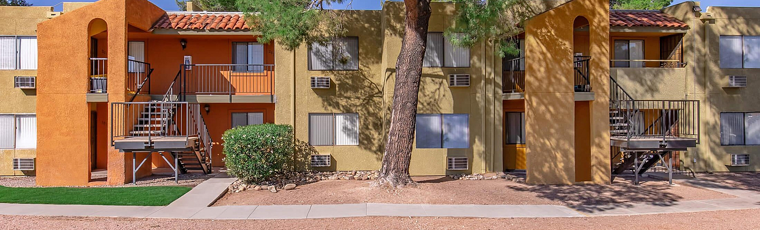 Inviting apartment complex with vibrant orange and yellow exterior, surrounded by lush greenery and mature trees.