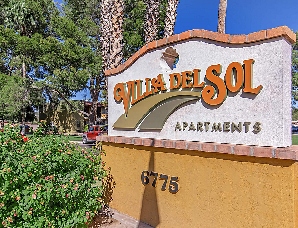 Inviting entrance sign for Villa Del Sol Apartments surrounded by lush greenery and vibrant flowers, showcasing a welcoming community ambiance.