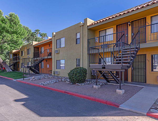 Charming apartment complex with modern two-story buildings, vibrant facade, and scenic green landscaping under a clear blue sky.