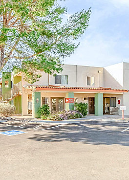 Sunset Vista Apartments exterior with modern architecture, vibrant landscaping, and ample parking under blue skies.