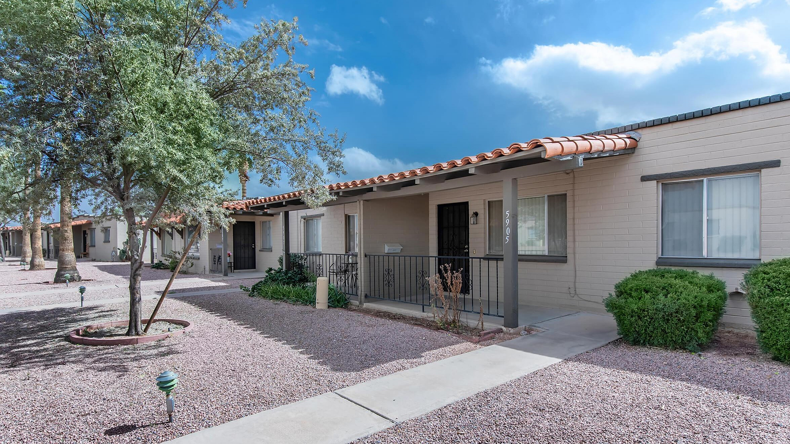 Charming single-story apartment with a welcoming porch, nestled under clear blue skies and surrounded by desert landscaping.
