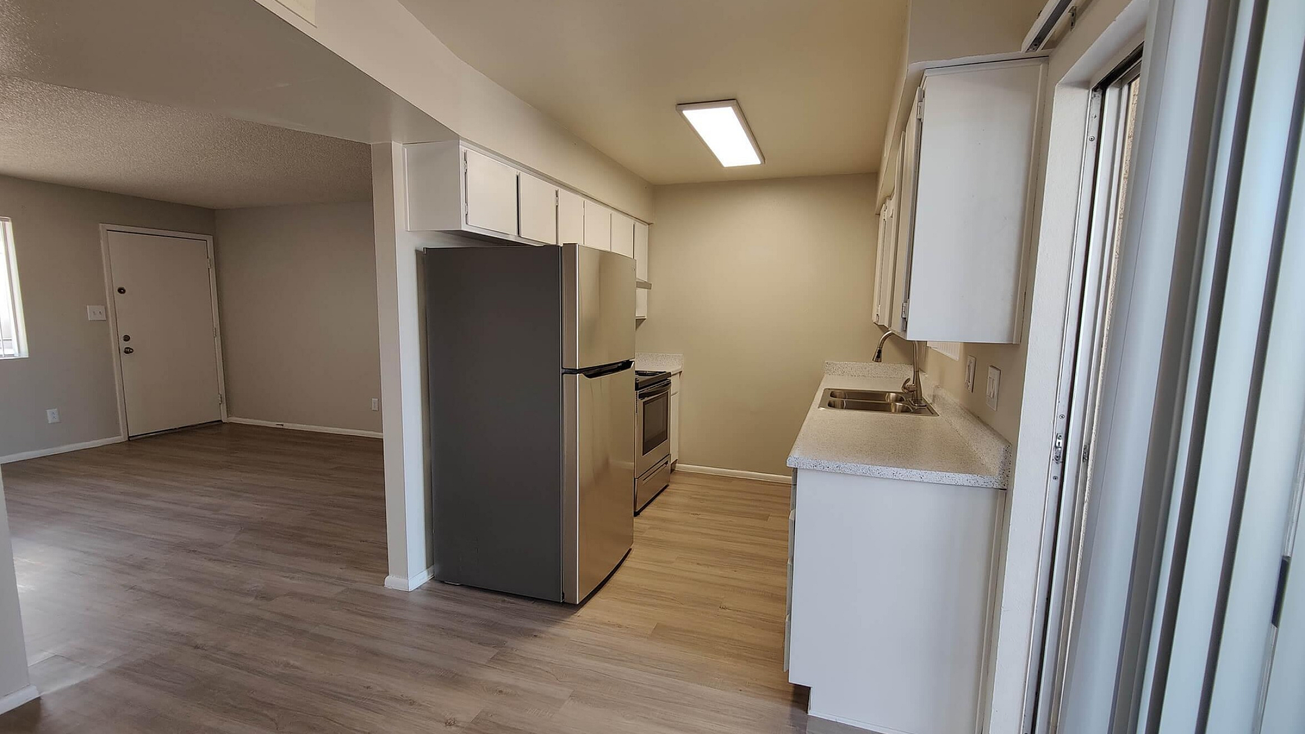 Modern apartment kitchen with stainless steel appliances, bright cabinetry, and warm wood flooring opening into a spacious living area.