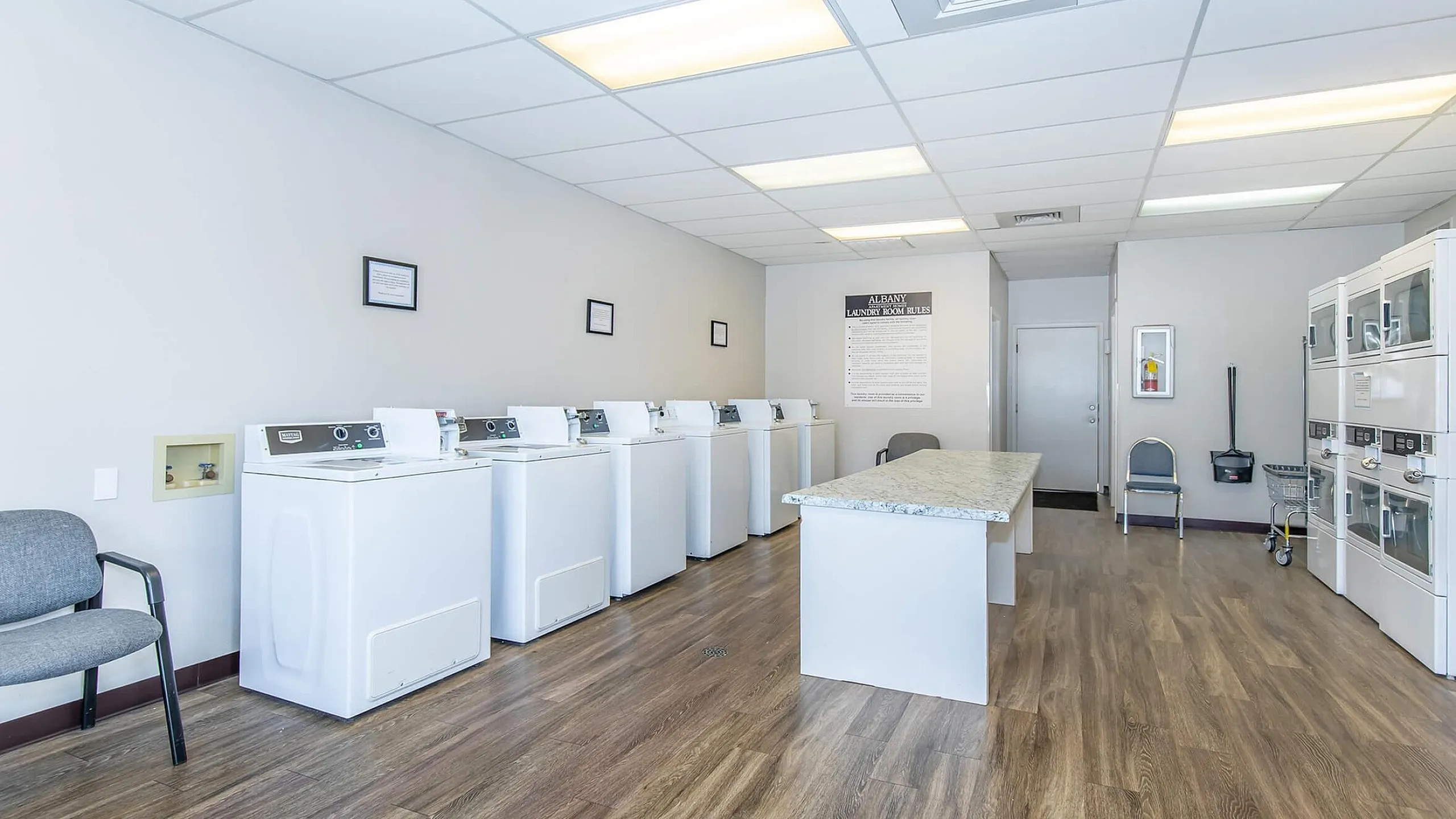 Bright and spacious laundry facility with modern washing machines, ample folding space, and sleek wood flooring.