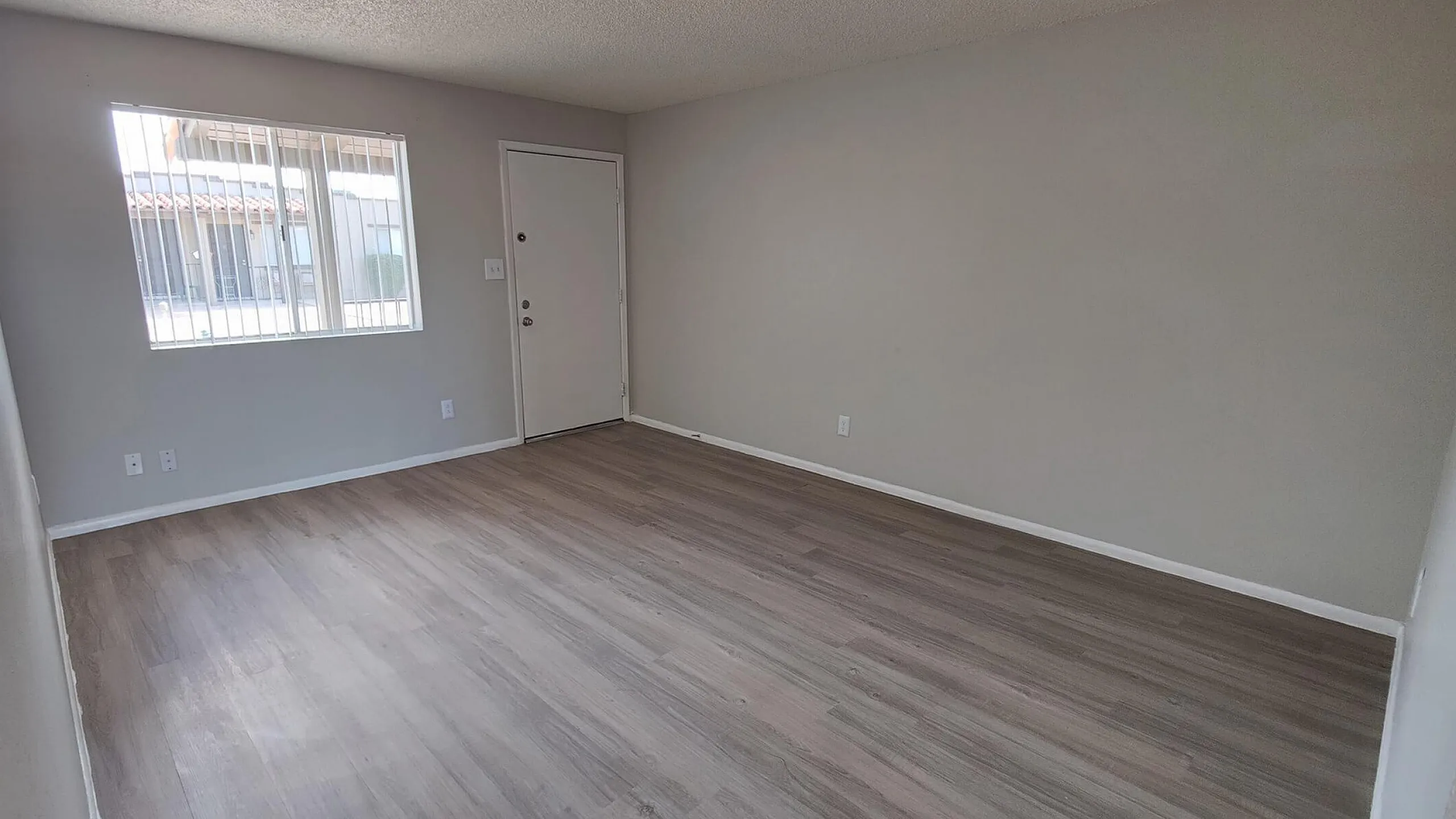 Bright living area with sleek laminate flooring and large window offering ample natural light.