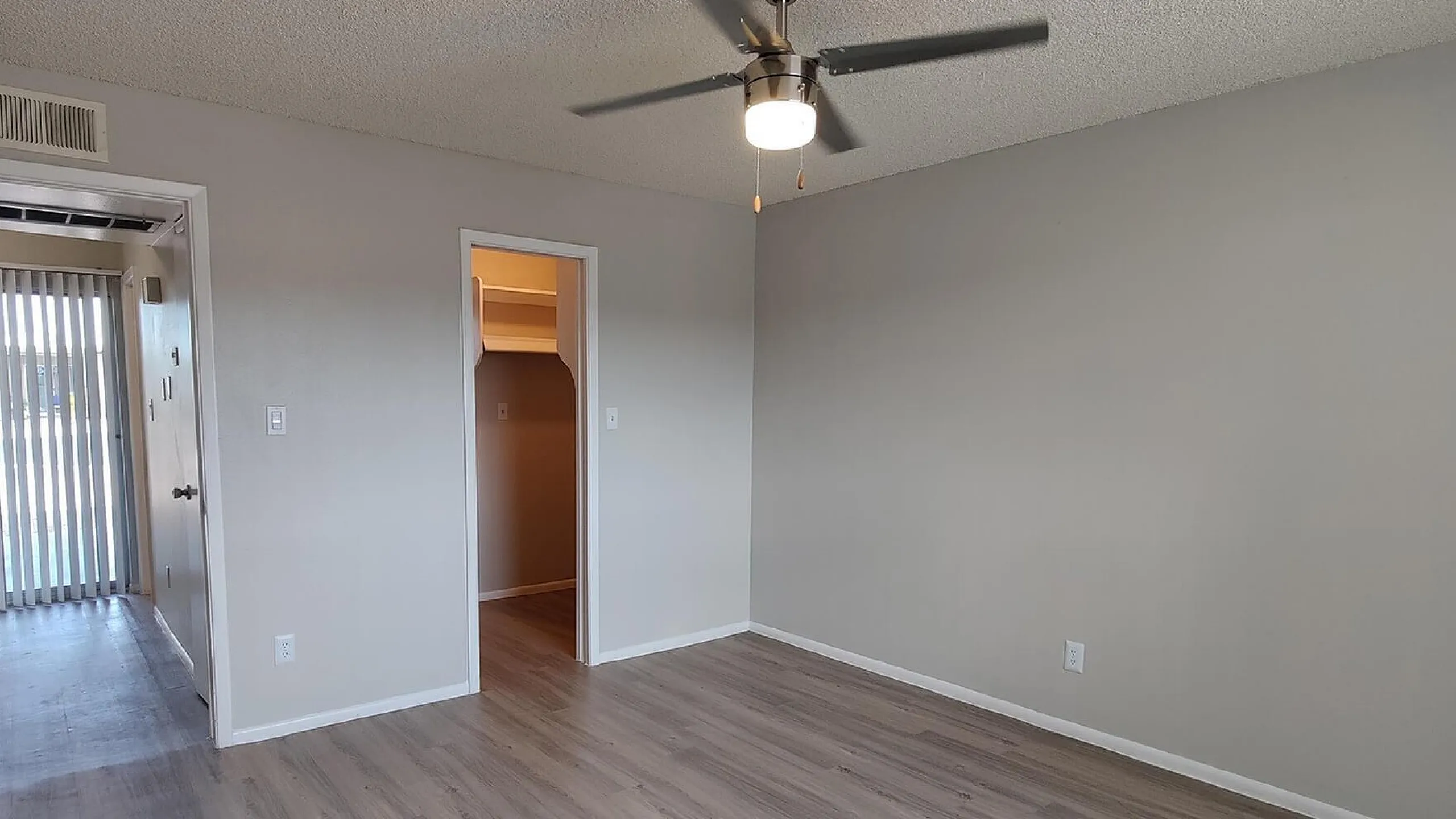 Spacious bedroom with elegant laminate flooring, ceiling fan, and ample natural light from glass doors, offering a tranquil and airy atmosphere.