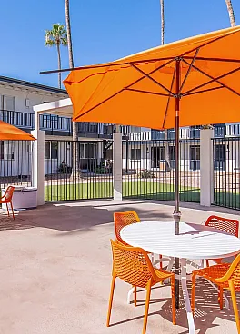 Vibrant outdoor seating area with orange umbrellas and chairs by a modern apartment complex, perfect for sunny relaxation.