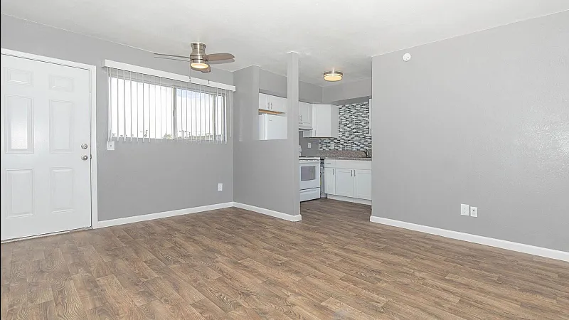 Modern apartment with open layout, featuring stylish hardwood floors, a ceiling fan, and a sleek kitchen with a mosaic backsplash.