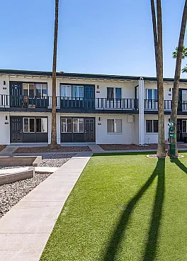 Charming courtyard view of a modern apartment complex featuring green lawns and tall palm trees, perfect for relaxation.