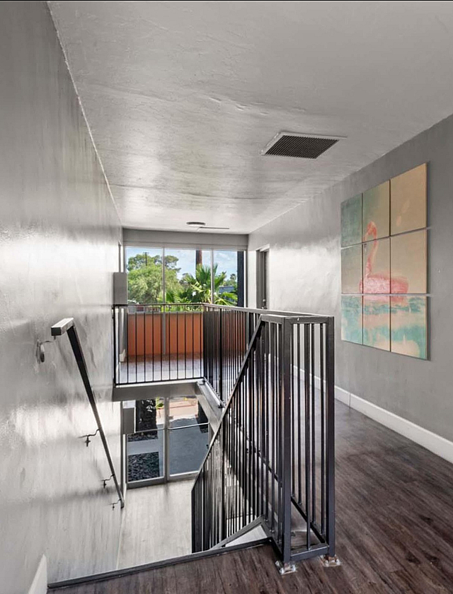 Bright and airy hallway featuring modern gray walls, a stylish flamingo artwork, and a staircase leading to floor-to-ceiling windows with lush greenery views.