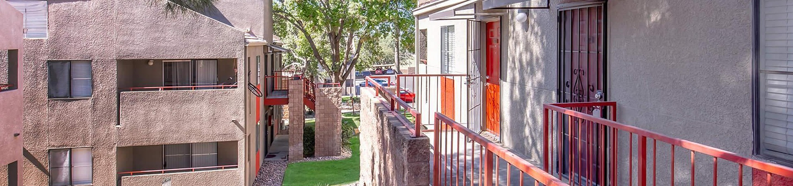 Charming apartment exterior with a vibrant red railing and lush green surroundings, offering a serene and inviting atmosphere.
