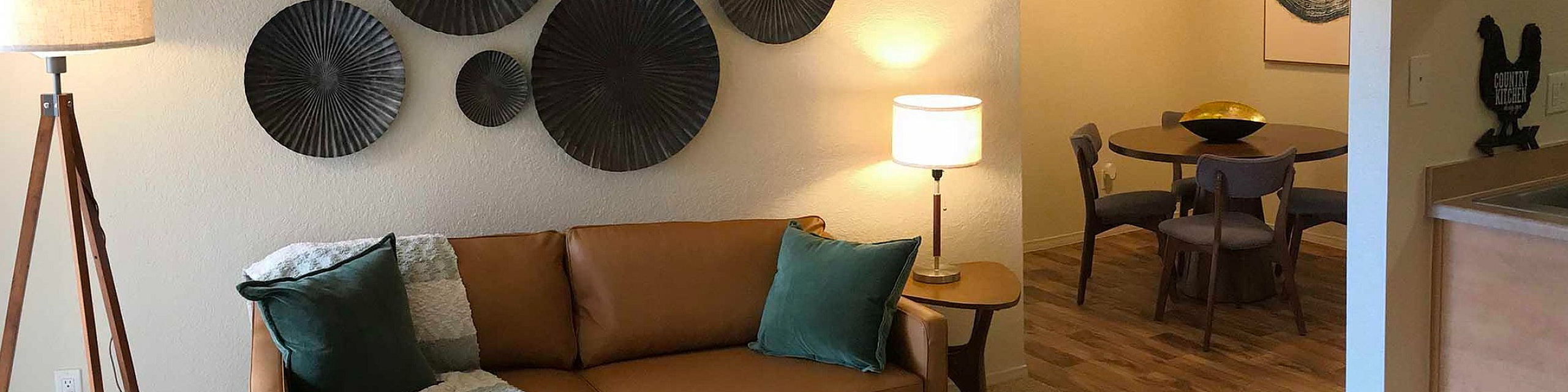 Cozy living room with a stylish brown sofa, elegant wall art, and warm lighting leading into a charming dining area.