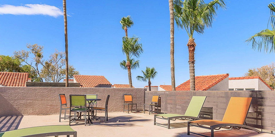 Chic rooftop patio with modern lounge chairs, vibrant seating, and lush palm trees under a clear blue sky.