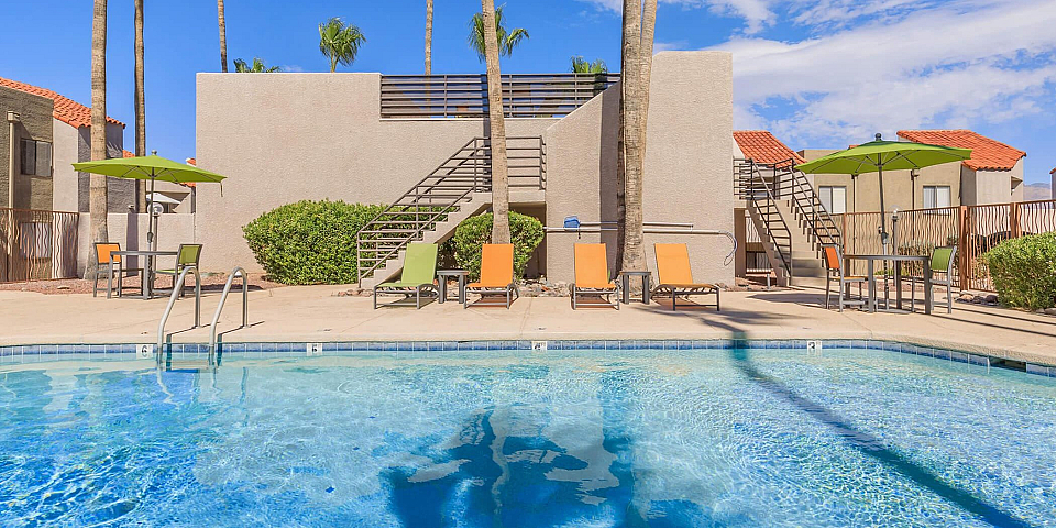 Inviting outdoor pool area with vibrant lounge chairs and umbrellas, set against a backdrop of clear blue skies and lush palm trees.