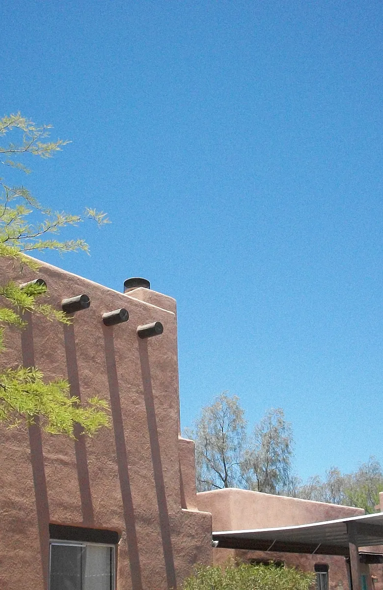 Charming stucco building with desert architectural style under a bright blue sky, accented by lush greenery.
