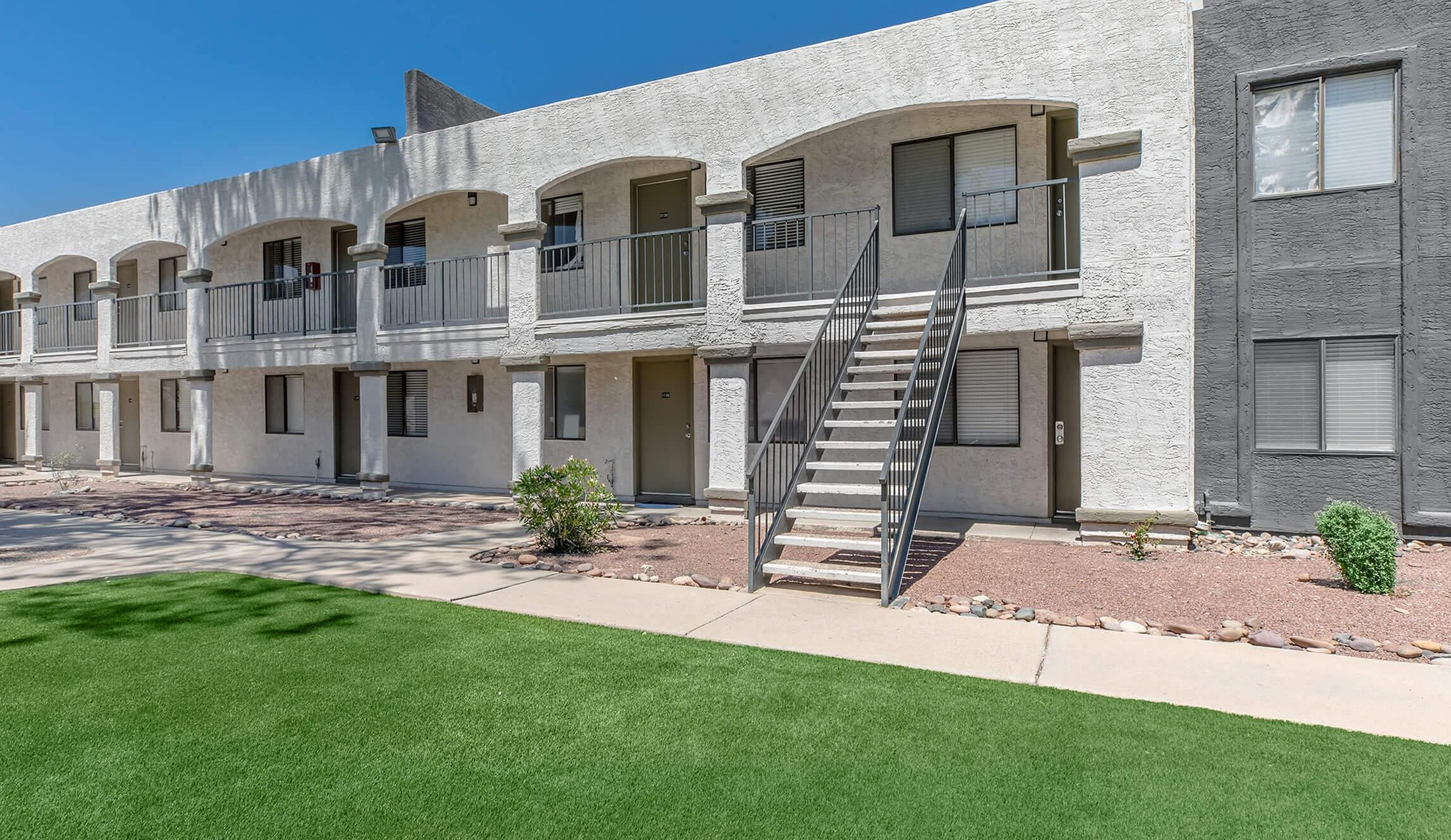 Modern apartment complex with stylish architecture, featuring a two-story building, lush green lawn, and inviting entrance.