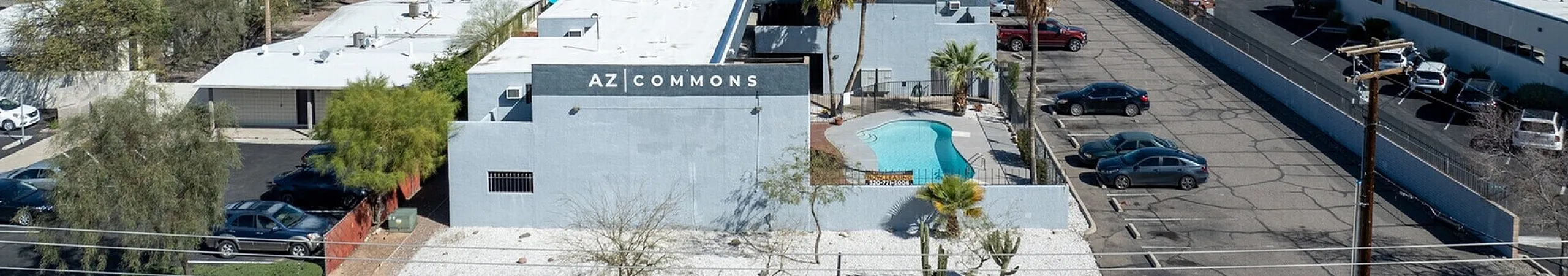 Scenic aerial view of AZ Commons with a refreshing pool, surrounded by mountains and lush palm trees under a clear blue sky.