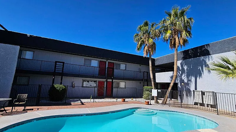 Inviting apartment courtyard with a sparkling pool, surrounded by palm trees and modern two-story buildings under a clear blue sky.