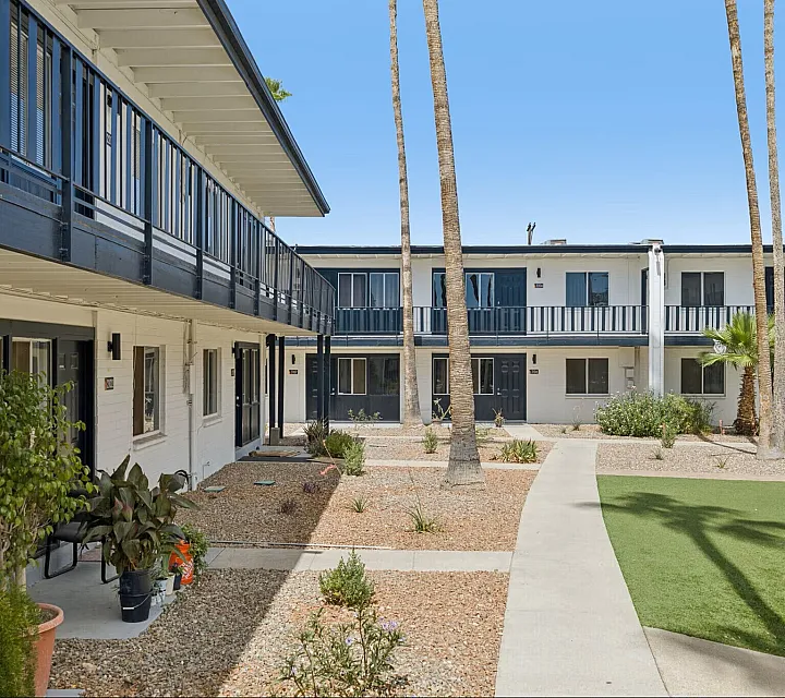 Charming courtyard view of modern apartment complex with lush landscaping and towering palm trees under a clear blue sky.