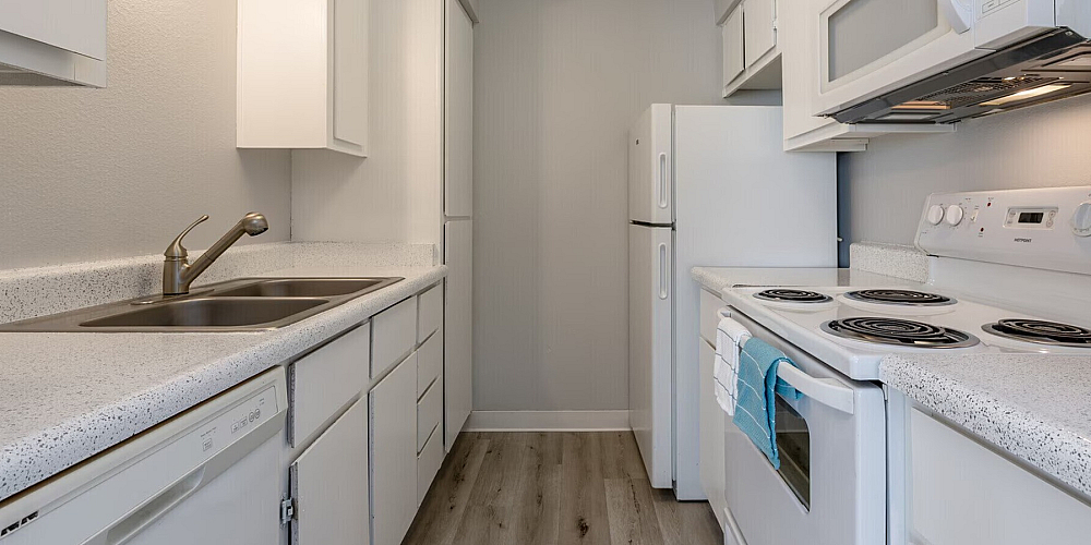 Modern galley kitchen with sleek white cabinetry, stainless steel sink, and energy-efficient appliances, perfect for culinary enthusiasts.