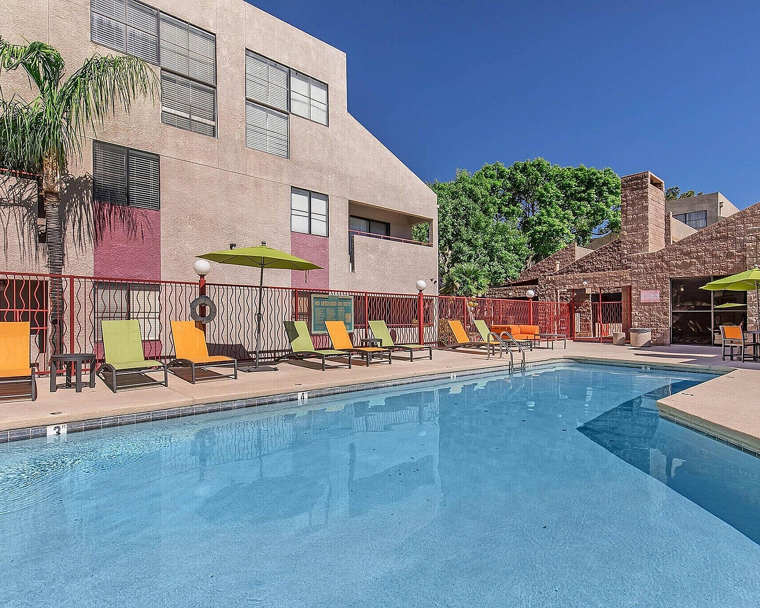 Inviting outdoor pool area with vibrant lounge chairs and shaded seating, surrounded by modern architecture.