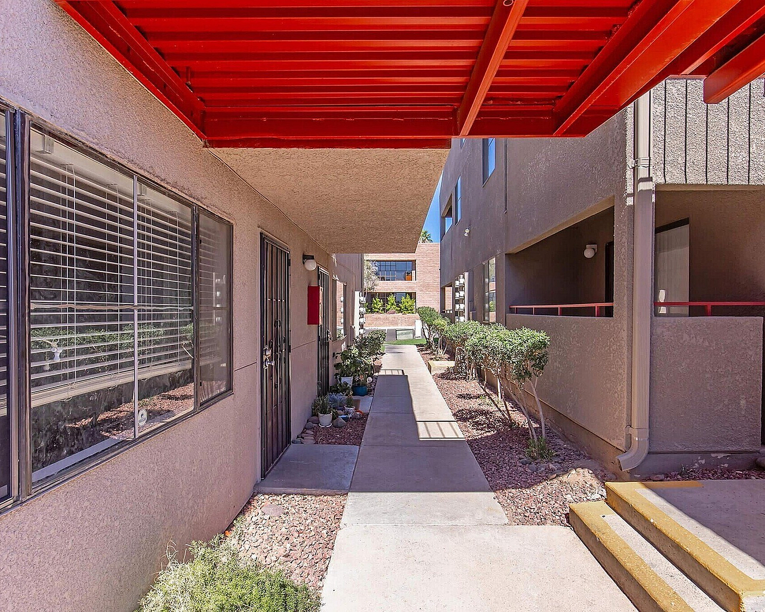 Inviting apartment entrance with modern red awning, pristine walkway, and lush greenery.