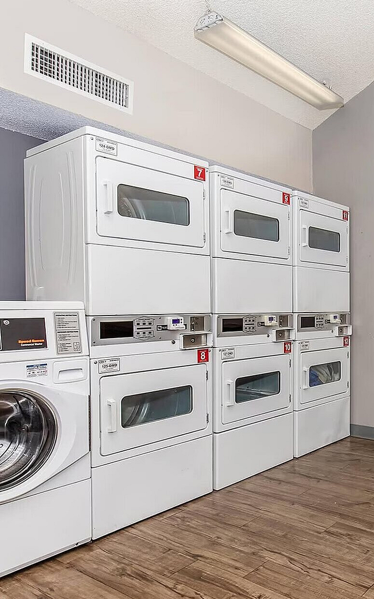 Modern communal laundry room featuring stacked washers and dryers on sleek wood flooring, perfect for convenient living.