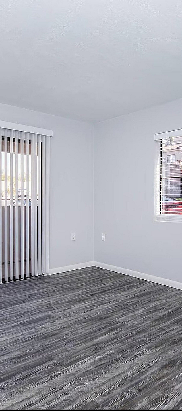 Bright, empty room with sleek gray laminate flooring, white walls, and vertical blinds covering a sliding door for ample natural light.