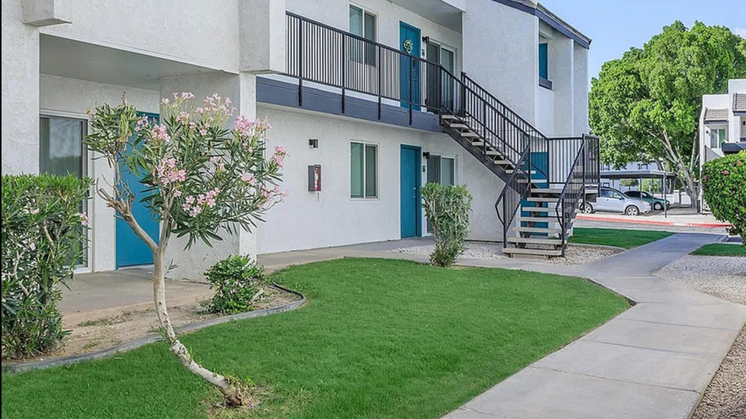 Modern apartment complex with lush green landscaping, accented by flowering plants and spacious balconies.