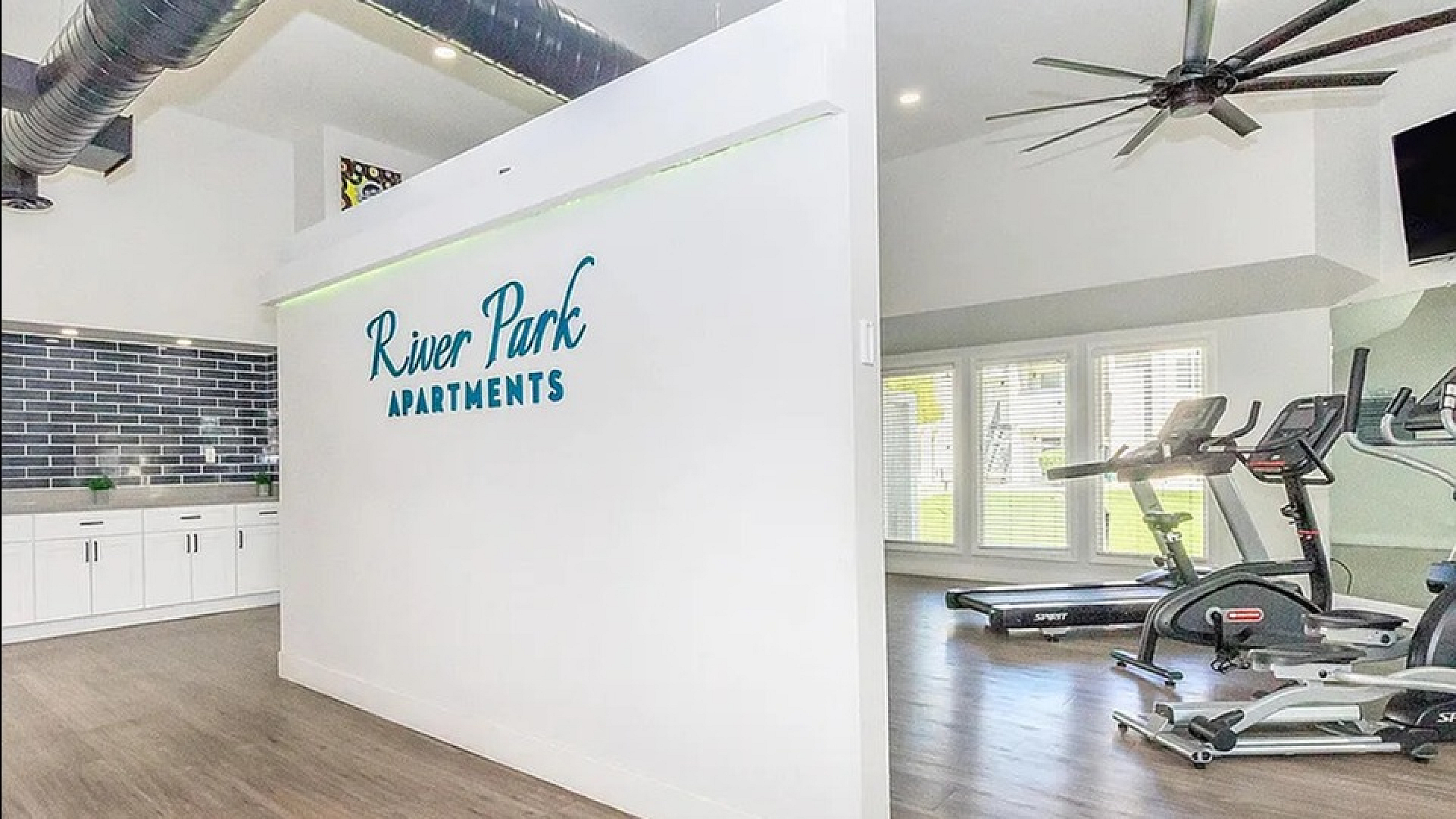 Bright and modern fitness area at River Park Apartments, featuring state-of-the-art exercise equipment and sleek wood flooring.