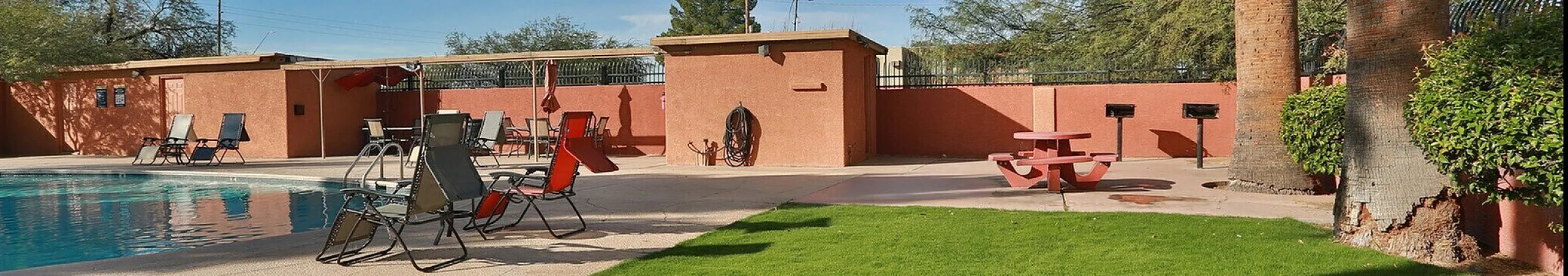 `Outdoor pool with lounge chairs, green lawn, and palm trees at San Simeon Apartments in Tucson, AZ`