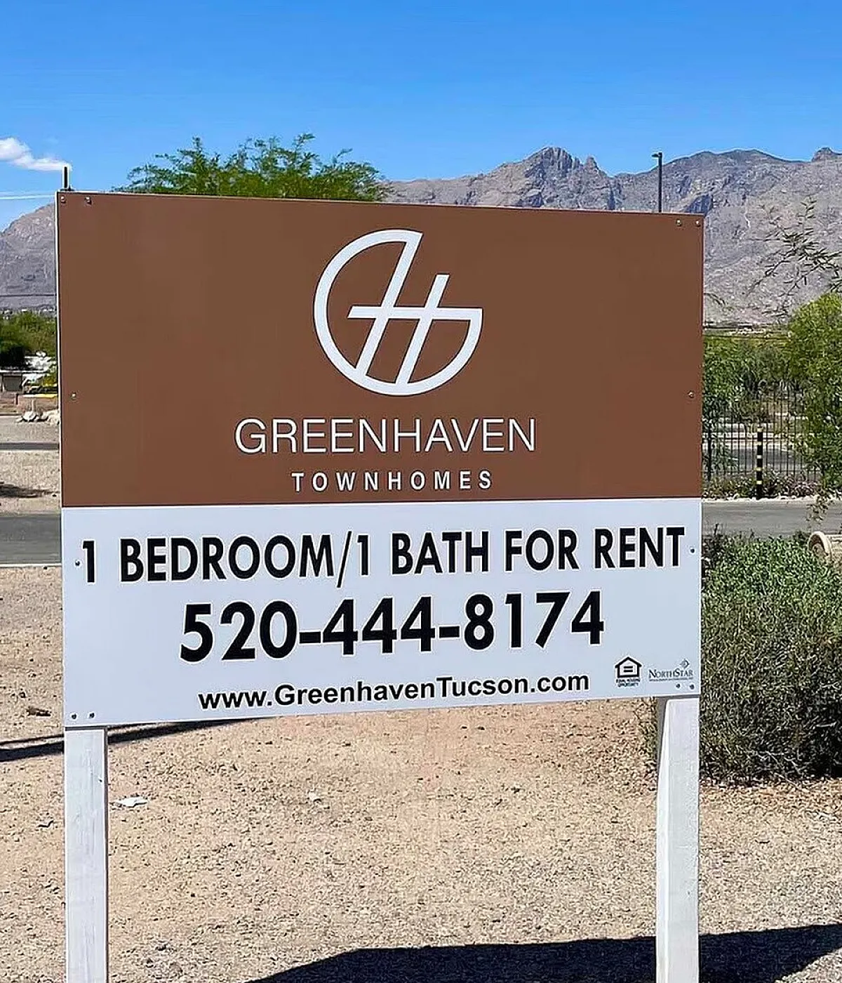 Greenhaven Townhomes sign advertising charming 1 bedroom, 1 bath for rent, set against a scenic desert mountain backdrop.
