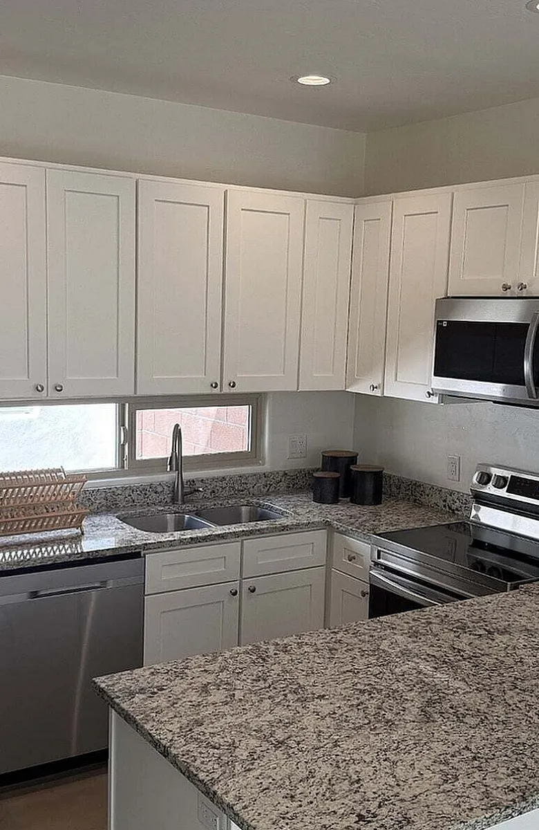 Modern kitchen featuring sleek stainless steel appliances, granite countertops, and pristine white cabinetry creating a stylish and functional cooking space.