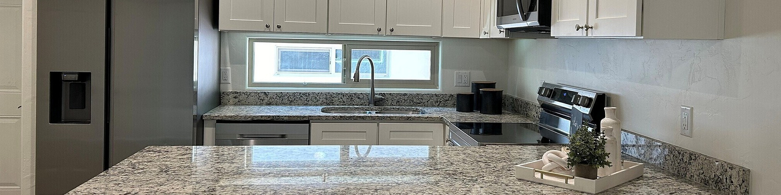 Modern kitchen with sleek stainless steel appliances, granite countertops, and elegant white cabinetry offering a bright and inviting atmosphere.