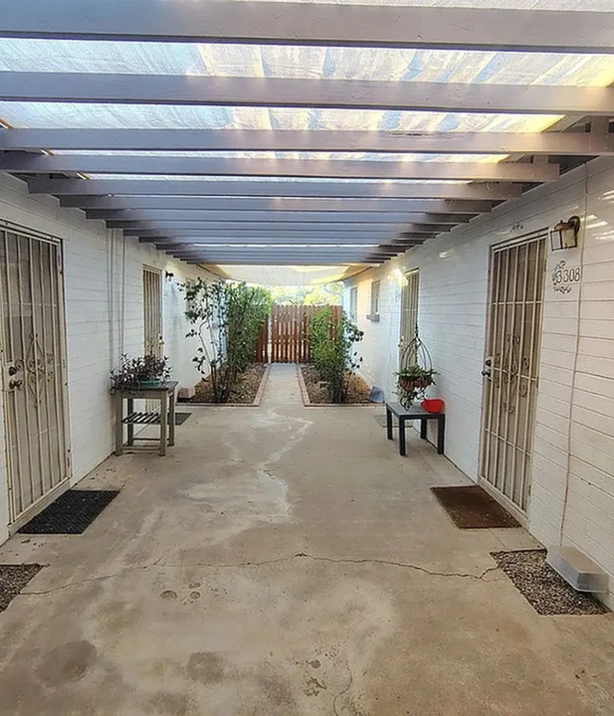 Charming covered walkway enhanced by natural light, featuring potted plants and secure entryways on a tranquil path.