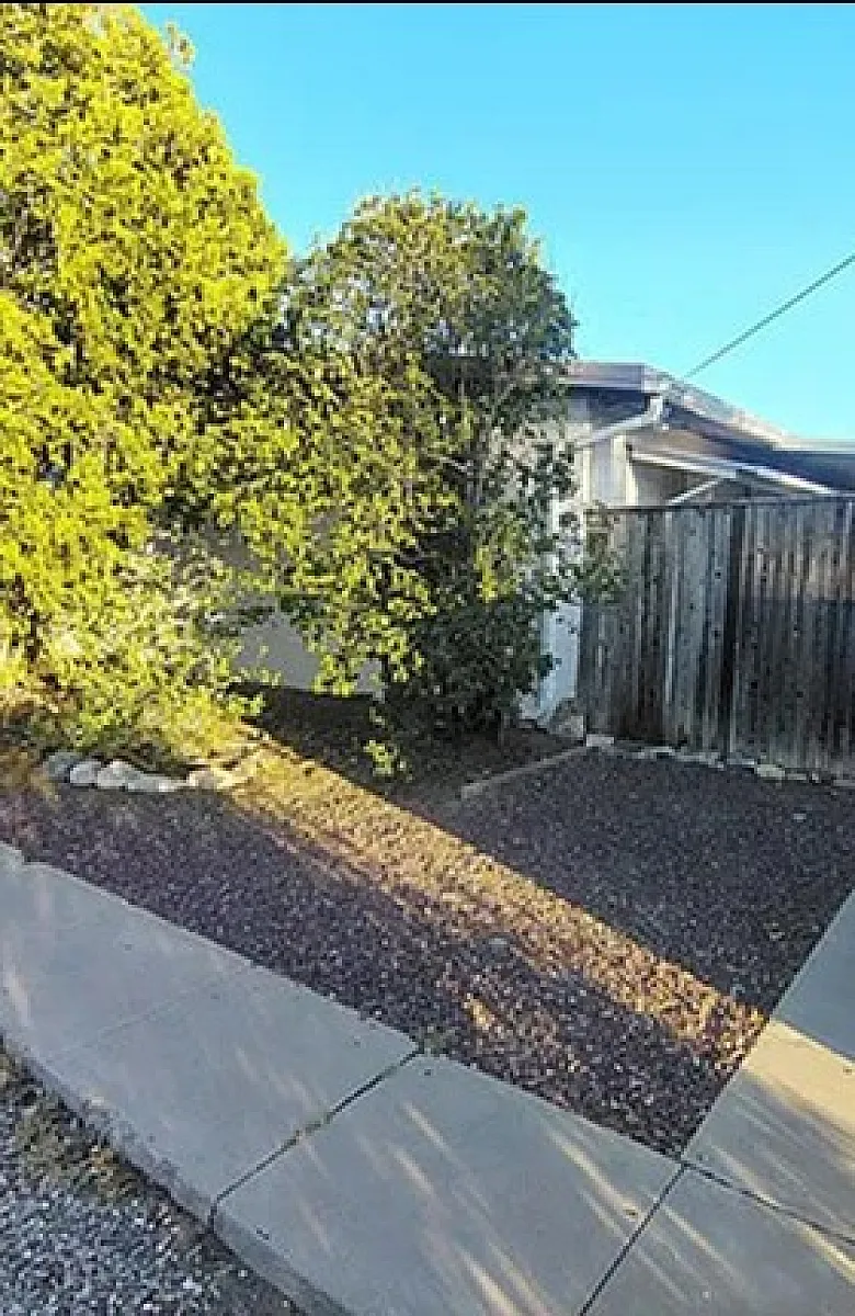 Charming fenced courtyard entry with lush greenery and bright blue sky in a serene setting.