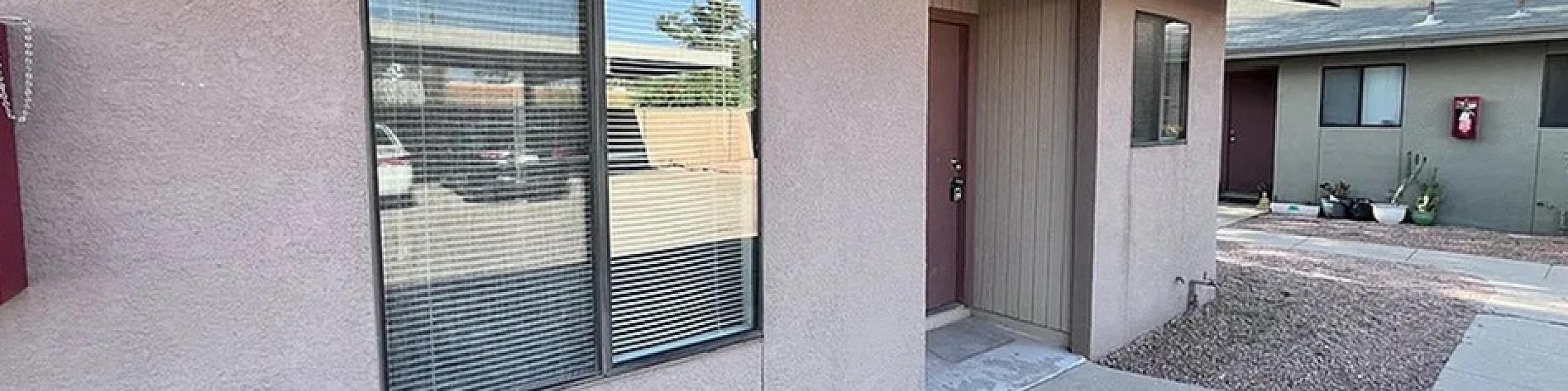 Charming apartment exterior with modern beige siding and large windows, set amidst a neat gravel landscape and a clear blue sky.