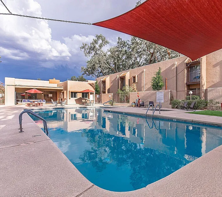 Inviting apartment complex featuring a refreshing swimming pool and modern outdoor seating under a vibrant canopy.