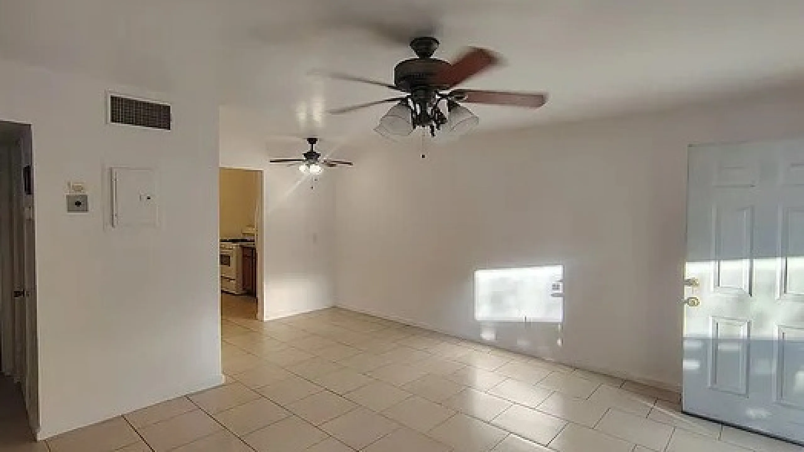 Bright living area with ceiling fans and tiled flooring, showcasing an inviting space leading to a modern kitchen.