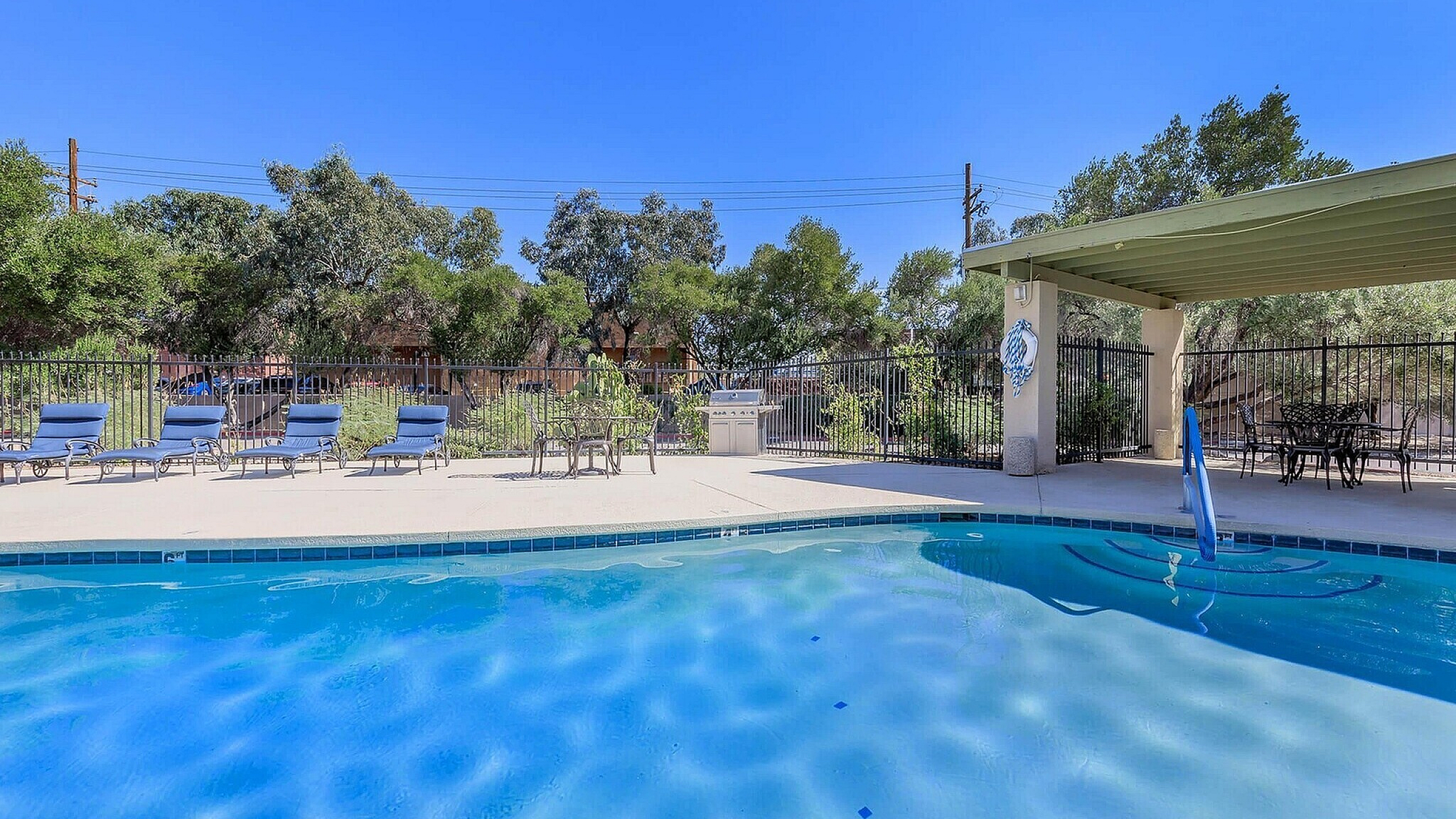 Inviting outdoor pool area with sun loungers, shaded seating, and lush greenery under a clear blue sky in Mountain Village Apartments.