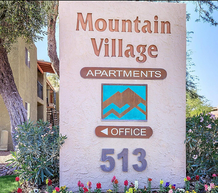 Inviting Mountain Village Apartments sign surrounded by vibrant landscaping and a tree-lined path, offering a welcoming community atmosphere.