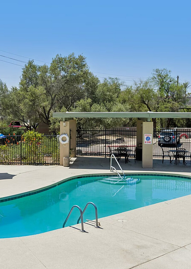 Inviting outdoor pool area with stylish blue loungers, shaded by lush greenery and a vibrant umbrella, perfect for relaxation.