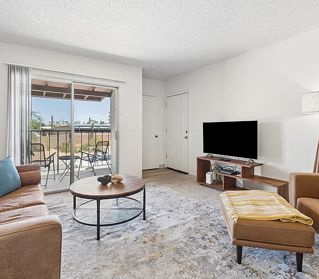 Bright and modern living room with cozy seating, large glass doors, sleek TV setup, and access to a charming patio area.
