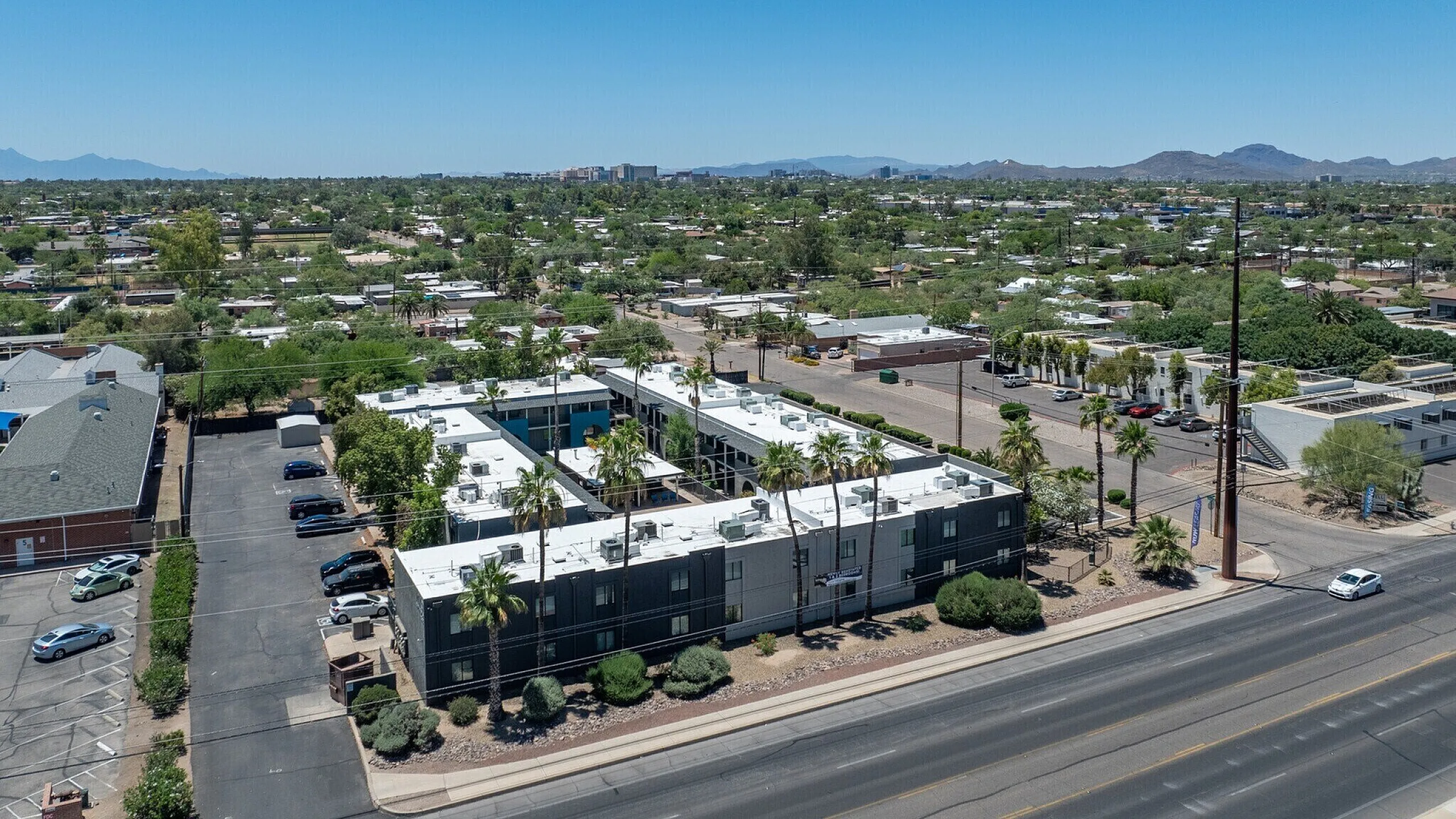 Aerial view of a modern apartment complex surrounded by lush greenery and mountain views, showcasing a well-maintained exterior and nearby amenities.