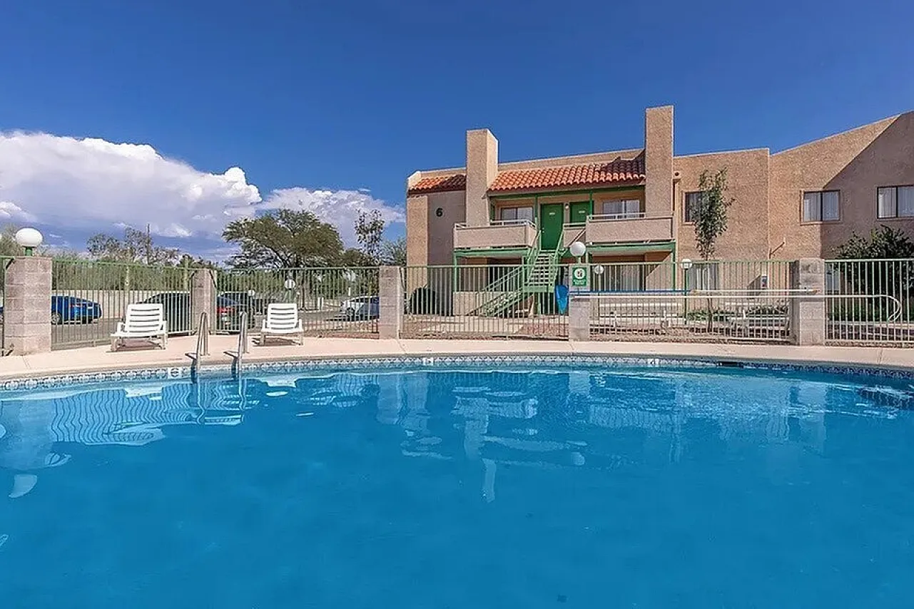 Inviting apartment pool area with crystal-clear water, surrounded by comfortable loungers, and a charming building with a warm, sunny facade.