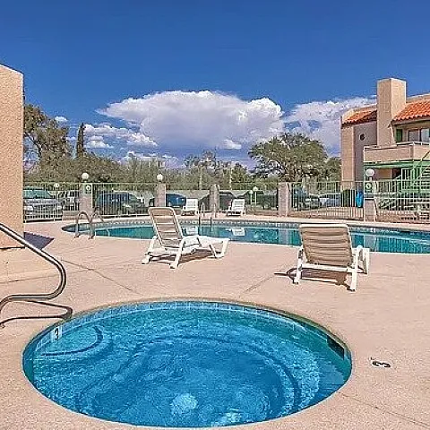 Inviting apartment complex with a crystal-clear swimming pool and hot tub, surrounded by lounge chairs for ultimate relaxation under a bright blue sky.