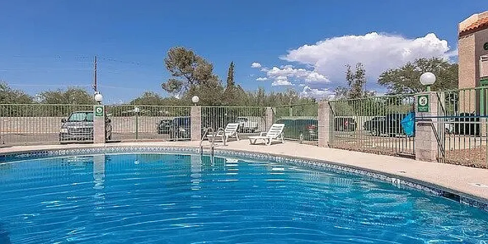 Inviting outdoor pool area with clear blue water, surrounded by sun loungers and lush greenery under a bright sky.