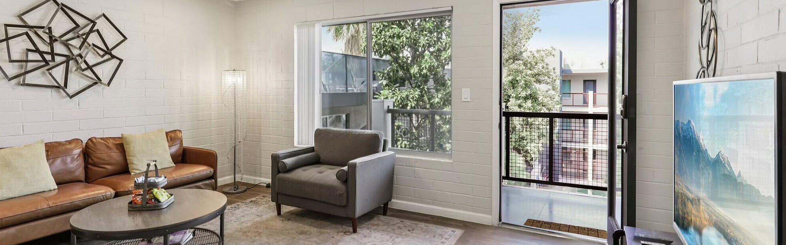 Bright and inviting living room with modern decor, featuring a stylish brown leather sofa, elegant armchair, and a large window opening to a picturesque balcony view.